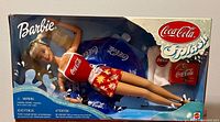 Front view of 1999 Coca Cola Splash Barbie in original packaging showing doll with red Coca Cola tank top, floral shorts, and blue inflatable pool float.