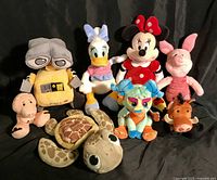 Group photo of nine assorted Disney Store plush toys including WALL-E, Daisy Duck, Minnie Mouse, Piglet, a turtle, and characters from The Lion King such as Timon and Pumbaa.