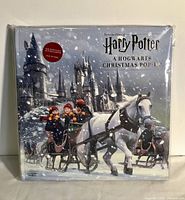 Front cover of the Harry Potter A Hogwarts Christmas Pop-Up Book, showing snowy Hogwarts castle and horse sleighs in winter scene