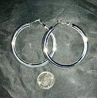 Front view of large silver hoop earrings with a dime for size reference
