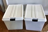 Two clear plastic wheeled storage bins with white lids and secured by black clips, shown side by side.