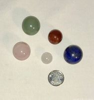 Five polished stone spheres of various colors and sizes alongside a dime for scale on a light surface.