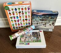 Three puzzle boxes and a rolled poster, showing the 'Cacti and Succulents', 'Welcome to Evergreen', and manga puzzles.