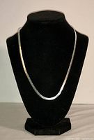 Silver herringbone necklace displayed on black velvet bust, showing full length and flat chain design.