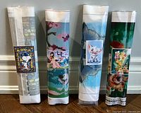 Four rolled diamond art kits in sealed plastic packaging on a wooden floor, showing the front printed sample images.