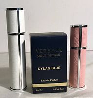 Front view of two travel perfume atomizers in white and pink faux leather and the Versace Dylan Blue perfume box between them.