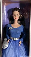 Close-up front view of Barbie doll showing blue shimmer gown, silver accessories, and dark brown hair.