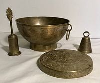 Front view of the brass bowl with handles, brass bell, candle snuffer, and trivet arranged together showing floral engravings and item details.