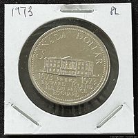 Reverse side of 1973 Canadian Prince Edward Island dollar coin showing the Legislature building with inscriptions "CANADA DOLLAR," "1873 PRINCE EDWARD ISLAND 1973," and "ILE DU PRINCE EDWARD." Coin in white cardboard flip.