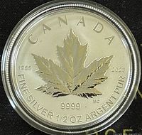 Front side of the Canadian Silver Maple Leaf coin showing the maple leaf, date range 1988 and 2023, and purity details (9999, 1/2 oz fine silver). Coin is in capsule.