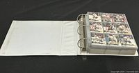 White 3-ring binder open to a page filled with multiple hockey cards in plastic sleeves.
