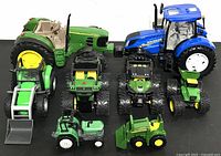 Photo showing all 8 John Deere and New Holland farm vehicles including tractors and utility vehicles arranged on white surface.