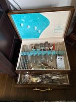 Full view of the opened wooden storage chest containing organized flatware in slots and a drawer with serving utensils