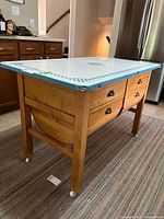 Three-quarter front view showing enamel top, wood base, drawers, casters