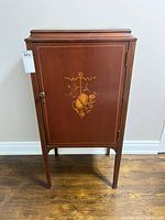 Front view of the antique wooden cabinet showing single door with decorative inlay and knob.