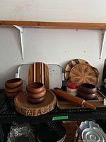 Wide view showing assortment of wooden bowls, trays, cutting boards, and a rolling pin arranged on shelves, highlighting natural wood finishes, bark edges, and inlay designs.