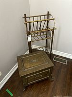 Brass rack behind a brass chest in a corner of a room on a wood floor.