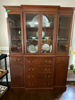 Front view of the wooden china cabinet with glass display doors showing shelves with dishes and the cabinet's drawers and doors below.