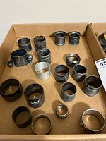 Photo of various metal and some brass napkin rings showing different sizes and etched patterns with some tarnish and patina.