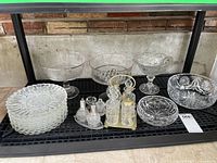 Full view of the lot displaying stacked small plates, two pedestal dishes, serving bowls, condiment set, and salt and pepper shakers on a black shelf.