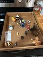 Wide view of cardboard box containing all miniatures including elephant figurines, decorated egg, small cups and other pieces