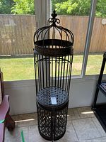 Tall black metal decorative bar stand with lattice patterned base and cage-style crown top