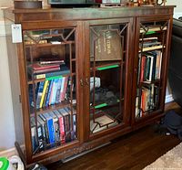 Front view of wooden display case showing three glass doors with decorative trim, interior shelves with books inside (contents not included).