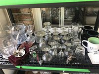 Full view of the collection showing multiple glassware items including wine glasses, pitchers, mugs, decanter, and silverplated tastevin cups on a shelf