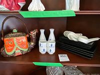 Camel-shaped colorful teapot with lid and woven handle alongside two Hakutsuru ceramic sake bottles, four sake cups, black trays and white spoons