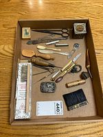 Box containing mixed antique and vintage tools including scissors, letter opener, small metal box, ivory or bone handled tools, small metal curiosities, and comb.