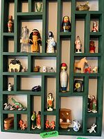 Full view of green wood shelf filled with various miniature figurines including animals, traditional dolls, and glassware