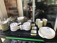 Overview of ceramic and porcelain kitchenware items arranged on rack including bowls, egg trays, cups and saucers