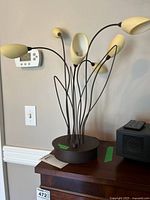 Photo of the lamp powered off showing cream flower-petal shaped bulb sockets with black metal stems emerging from round dark base.