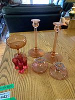View of the entire set: two tall pink candle holders, one pink compote/coupe, five small pink cordial glasses, and two pink candlesticks with beaded rims on a wooden table.