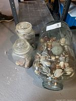 Three glass jars filled with assorted natural rocks and stones in a basement setting.