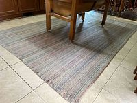 Full view of woven rug on tiled floor with a wooden table partially on top.