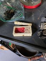 Closeup of small carved bone or ivory piece and small carved red fabric-lined box among shark teeth fossils and fossil pieces.