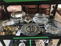 Overview of collection items arranged on a rack showing multiple silverplate serving trays, cups, and glass bowls.