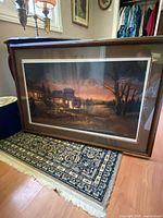 Framed print titled "Total Comfort" by Terry Redlin depicting a peaceful evening lakeside cabin scene, displayed on floor showing whole artwork and frame.