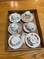 Photo showing six upside-down vintage bone china teacup and saucer sets in a box displaying their backstamp logos.