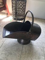 Metal coal scuttle shown from side angle displaying the handle and wide coal opening, with visible wear and age on surface.