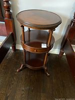Front angle view of round wood accent table showing top surface, middle drawer, and lower shelf with visible wear.