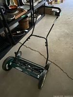 Green Yardworks reel mower showing full push handle and reel blades on concrete floor in storage area.