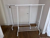 Photo of one white IKEA RIGGA rolling rack showing adjustable height holes, caster wheels, and lower slatted shelf.