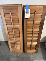 Eight rectangular pine wood window shutters stacked against a wall, some showing slight color variation.