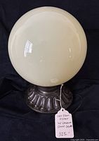Front view of charming antique cast iron light fixture with large creamy vaseline glass globe shade on ornate fluted base.