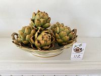 Full view of artichoke porcelain bowl filled with five faux artichokes from above.