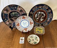 Wide shot showing five Asian decorative plates and dishes arranged on a wood surface with white background.