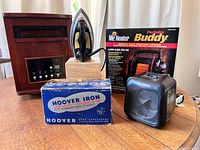 Lot photo showing LifeSmart woodgrain cabinet heater, Hoover vintage iron on wooden block, Mr. Heater Buddy propane heater box, and Pelonis DiscFurnace III compact fan heater.