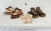 Shows all three pairs of baby shoes together: two sets are bronzed bookends, one set pink plaster shoes.
